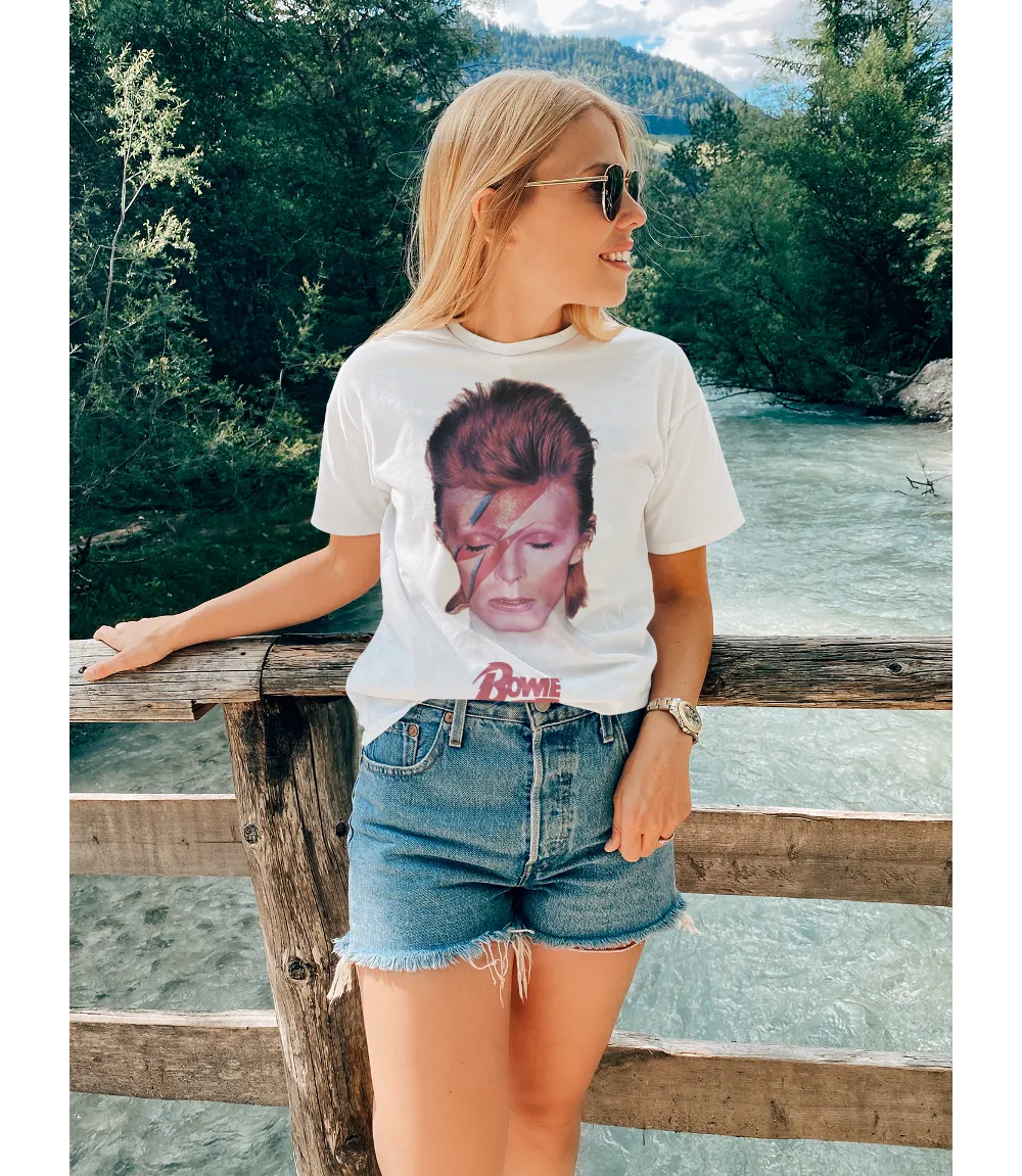 Woman wearing Unisex short sleeve white t-shirt featuring official David Bowie Aladdin Sane album cover design with Bowie text in red below / Retro Tees
